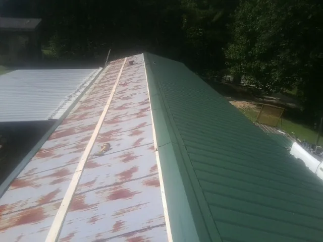 Old rusted panels beside newly installed green metal roofing — Wind Damage Roof Repair by Roofing Brothers in Bryceville