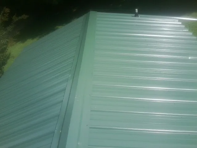 New green metal panels meeting at the ridge of a roof — Flat Roof Repair work by our crew in Bryceville